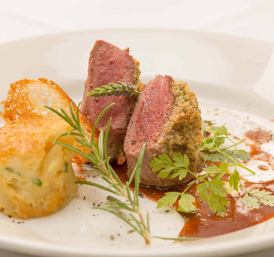 Gourmet dish with herb crust and side, garnished with fresh herbs