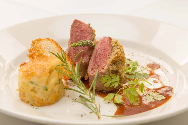 Pink roasted lamb fillet with herb crust © Kurt und Heidi Klingeisen Gourmet dish with herb crust and side, garnished with fresh herbs