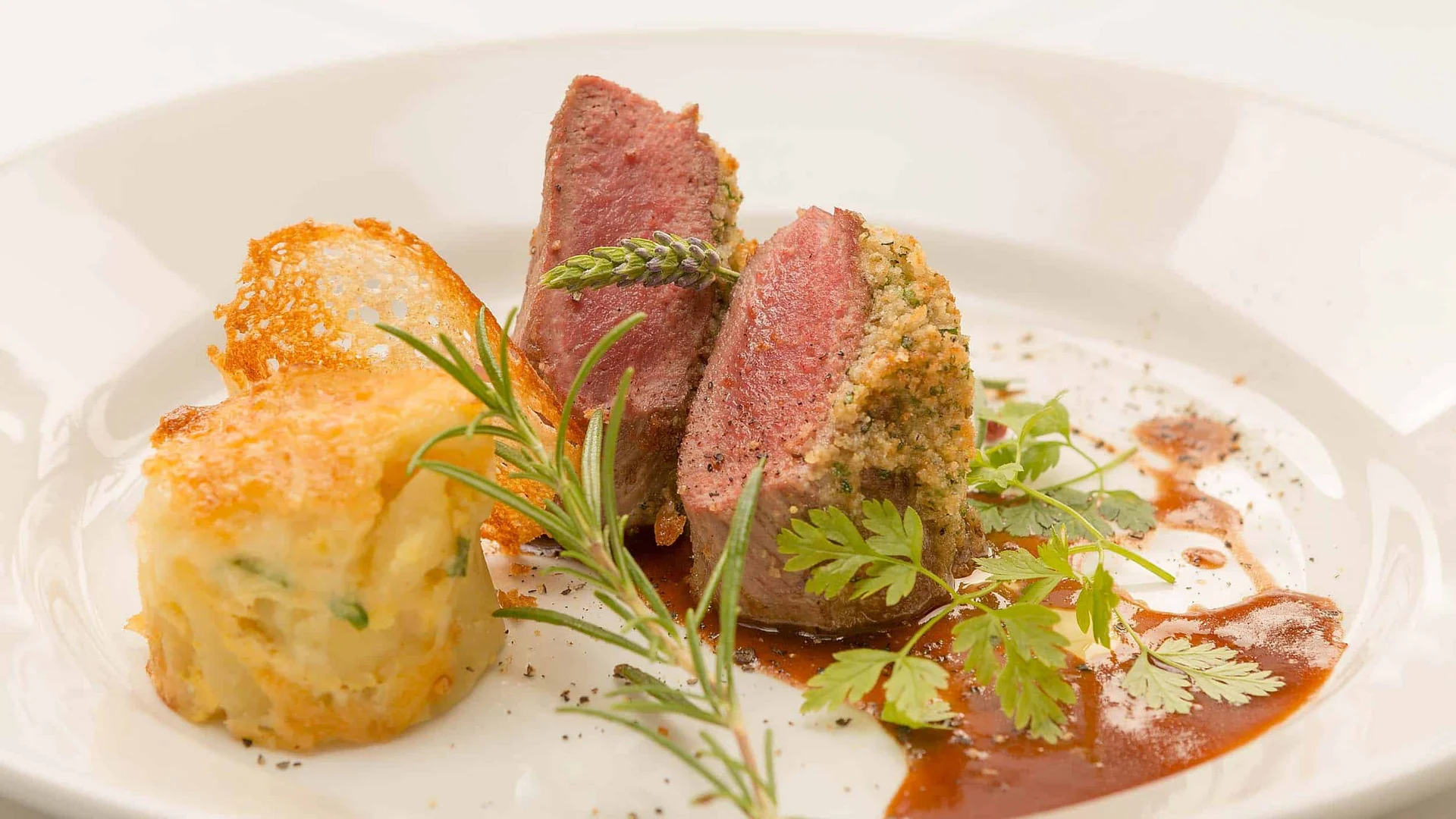 Gourmetgericht mit Kräuterkruste und Beilage, garniert mit frischen Kräutern