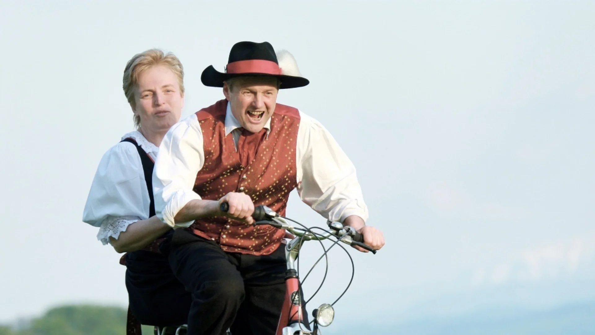 Mostbaron cycle route Man and woman in traditional clothes riding a bike in a blooming meadow
