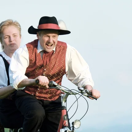 Mostbaron cycle route Man and woman in traditional clothes riding a bike in a blooming meadow