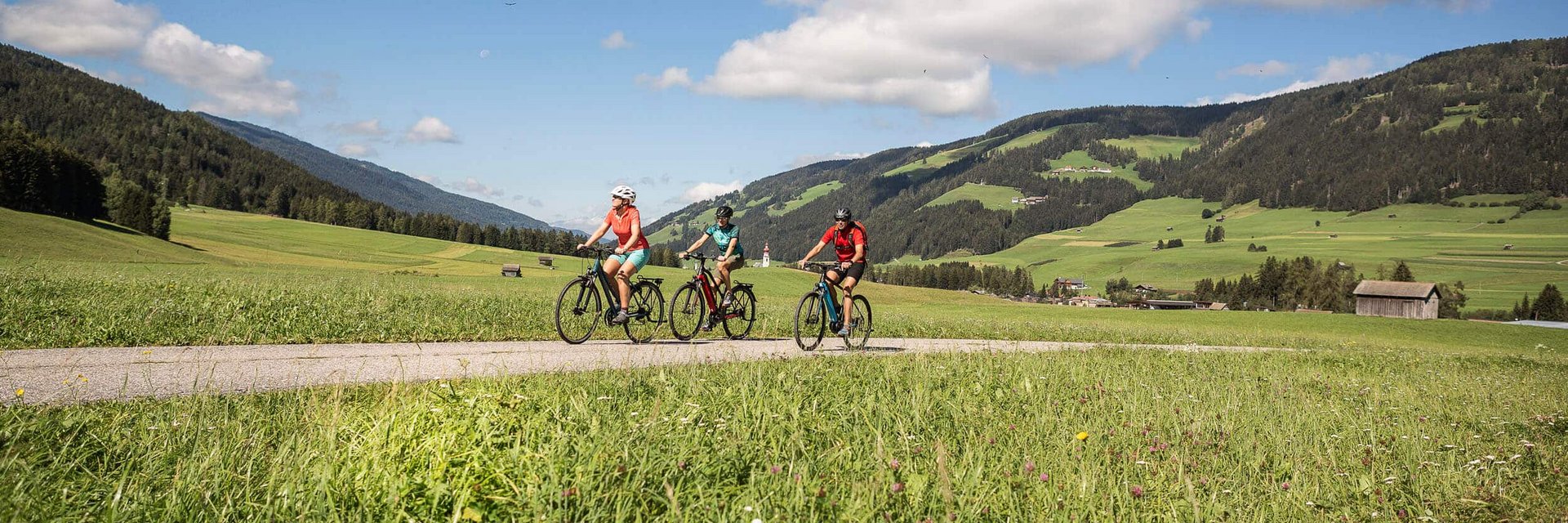 Three cyclists riding on a path through green meadows and mountains