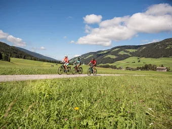 Villabassa - 3 Peaks Dolomites © Velontour Three cyclists riding on a path through green meadows and mountains