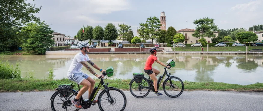 Zwei Radfahrer fahren an einem Fluss in einer Stadt vorbei