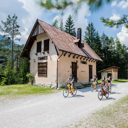 Family biking on a path past an old house in the forest