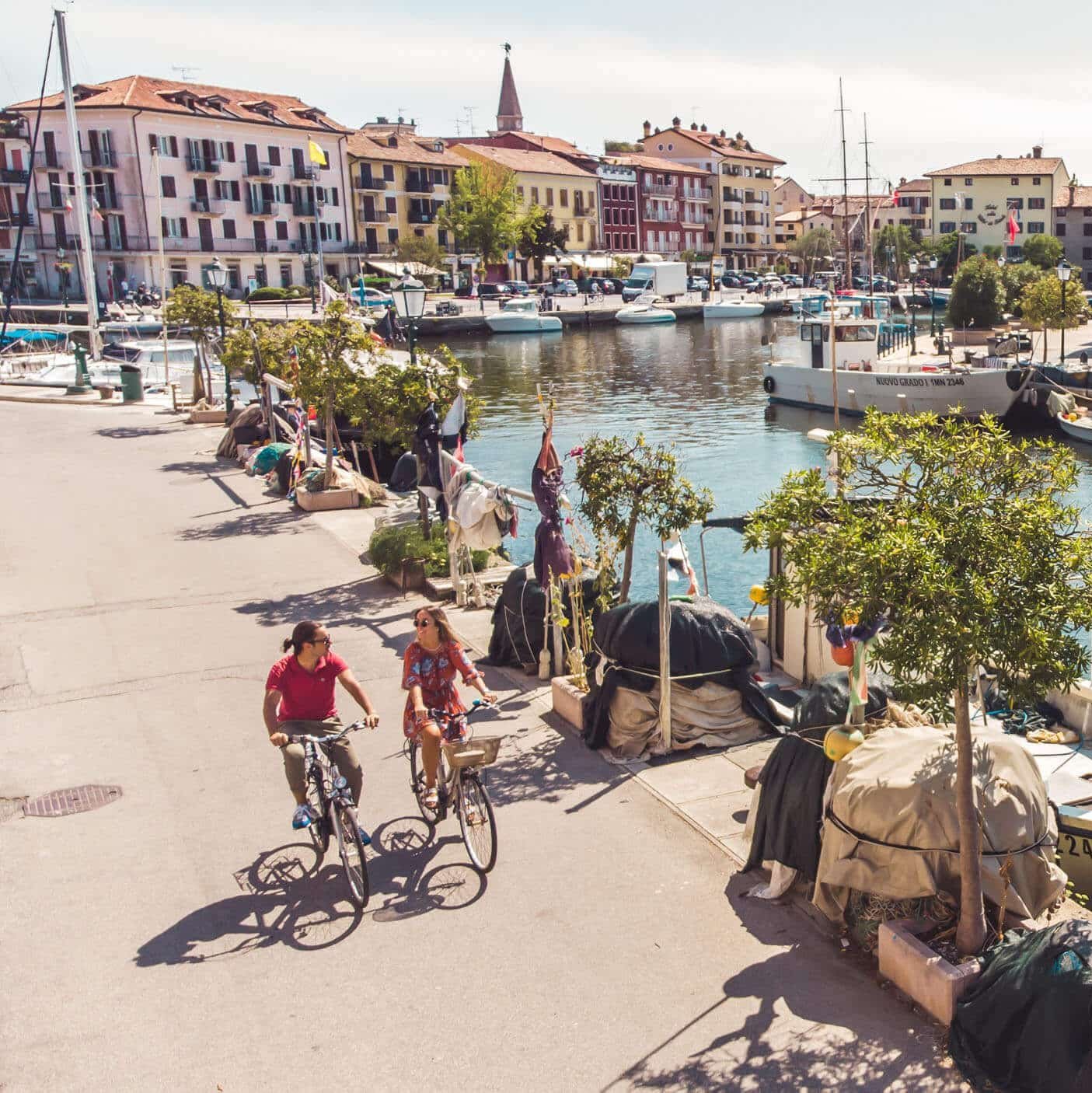 Zwei Radfahrer am sonnigen Kanal mit Booten und bunten Häusern