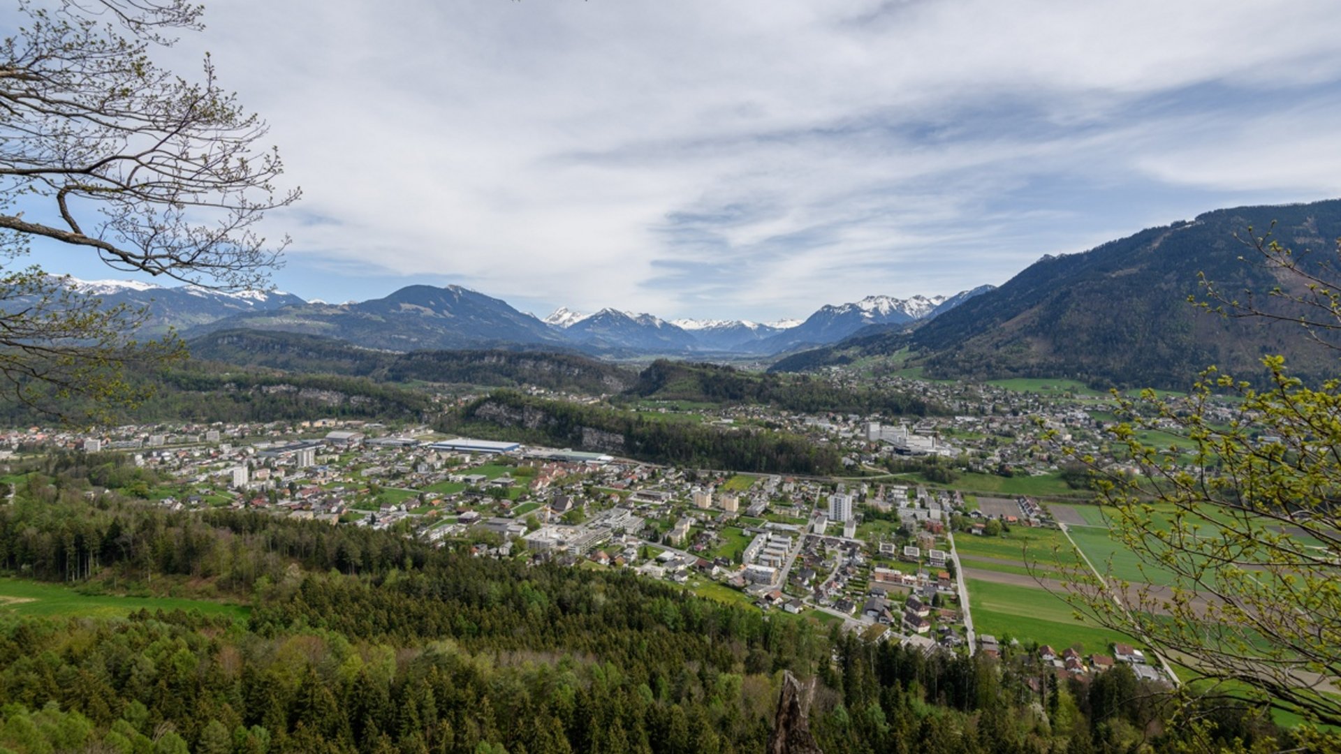 View of a town in a valley with forested hills and snow-capped mountains in the background