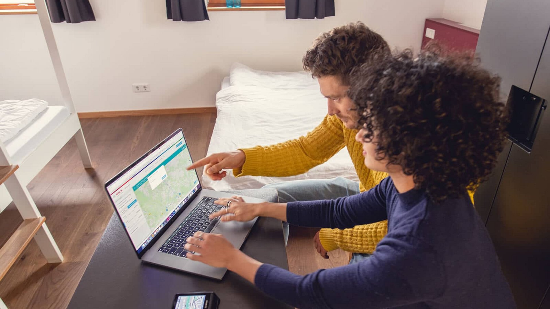 Two people looking at a map on a laptop in a simple room