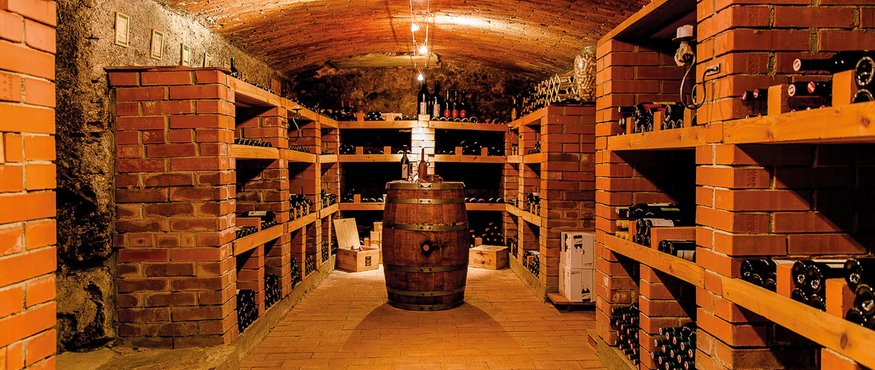 Wine cellar with brick floor, shelves of bottles and a barrel in the center