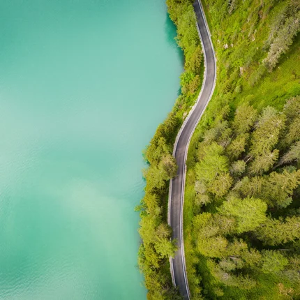 Luchtfoto van een kronkelende weg langs een groen bos en een turquoise meer
