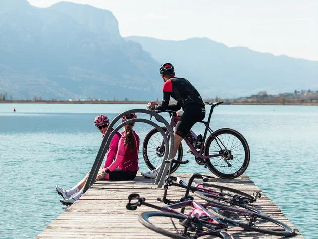 Kulinarisch unterwegs in Tramin © TV Kaltern am See - Felix Homann Drei Radfahrer auf einem Steg am See mit Bergen im Hintergrund