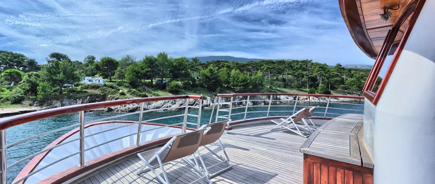 Boat deck with chairs overlooking forested shoreline under clear blue sky