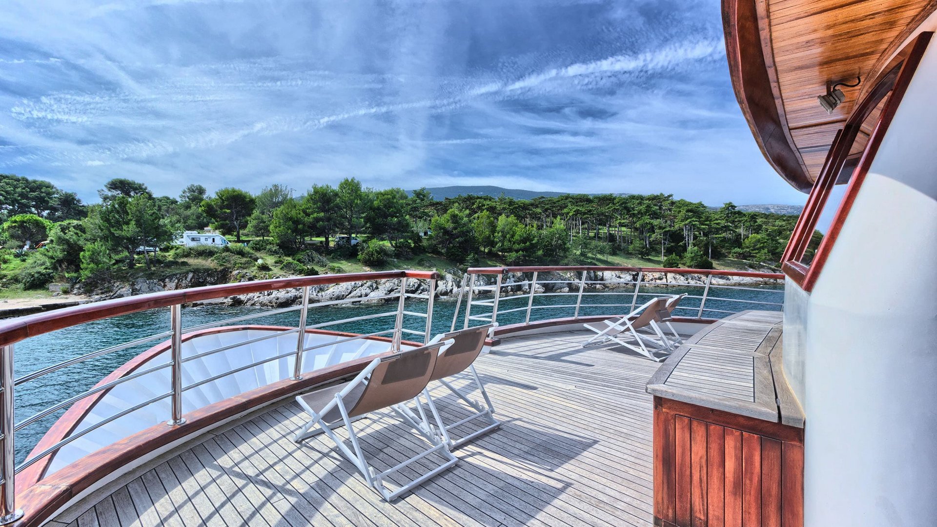 Boat deck with chairs overlooking forested shoreline under clear blue sky
