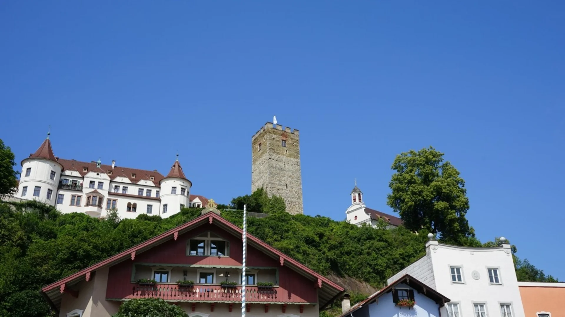 Historische Gebäude und Turm auf einem bewachsenen Hügel unter blauem Himmel