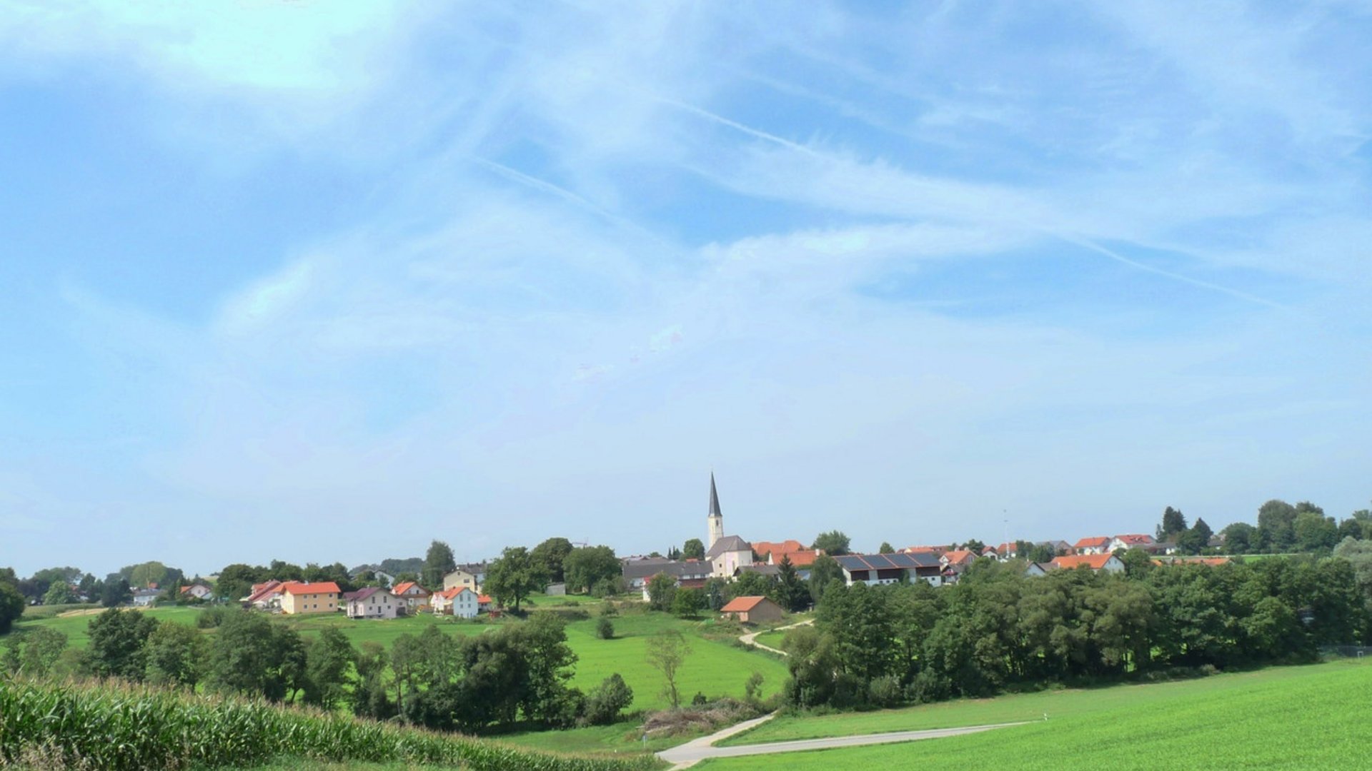 Village with church and green fields under a blue sky