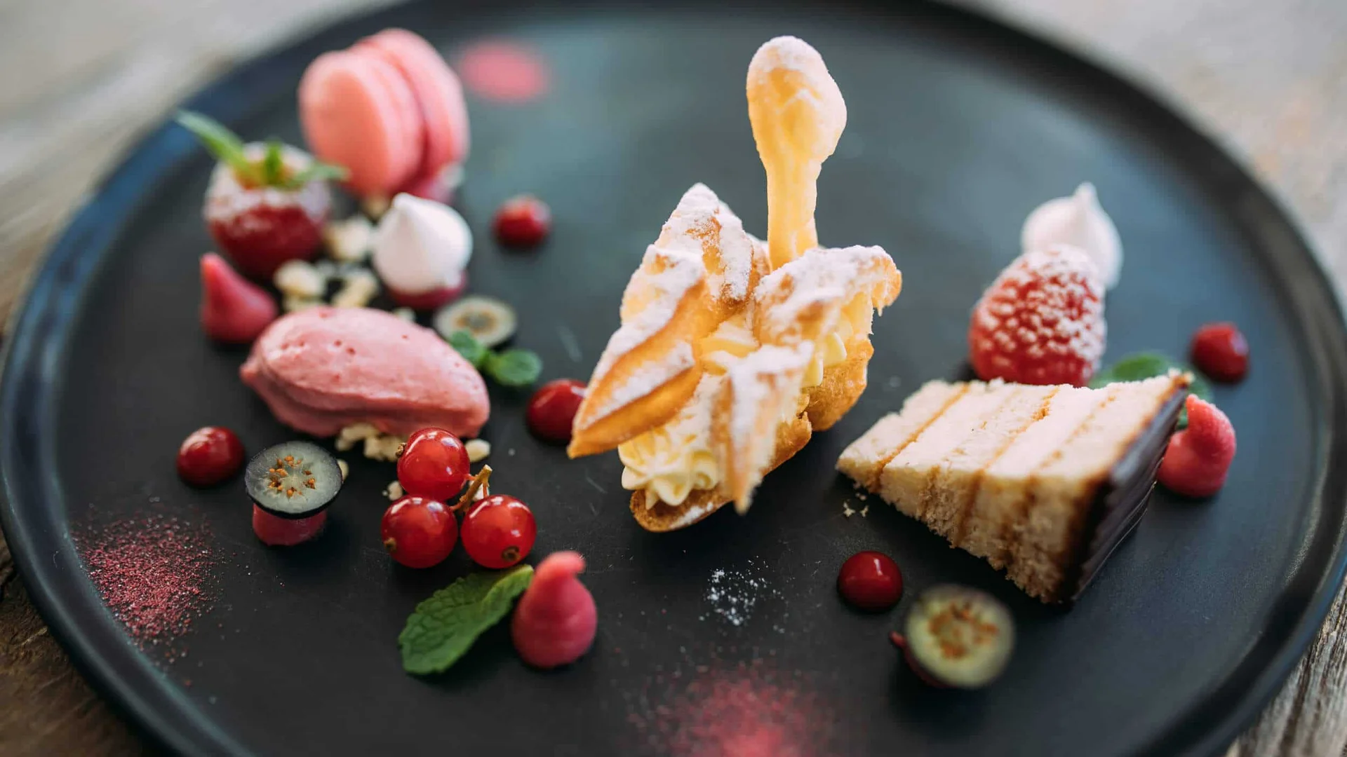 Assortment of fine desserts and fruits artfully arranged on a black plate