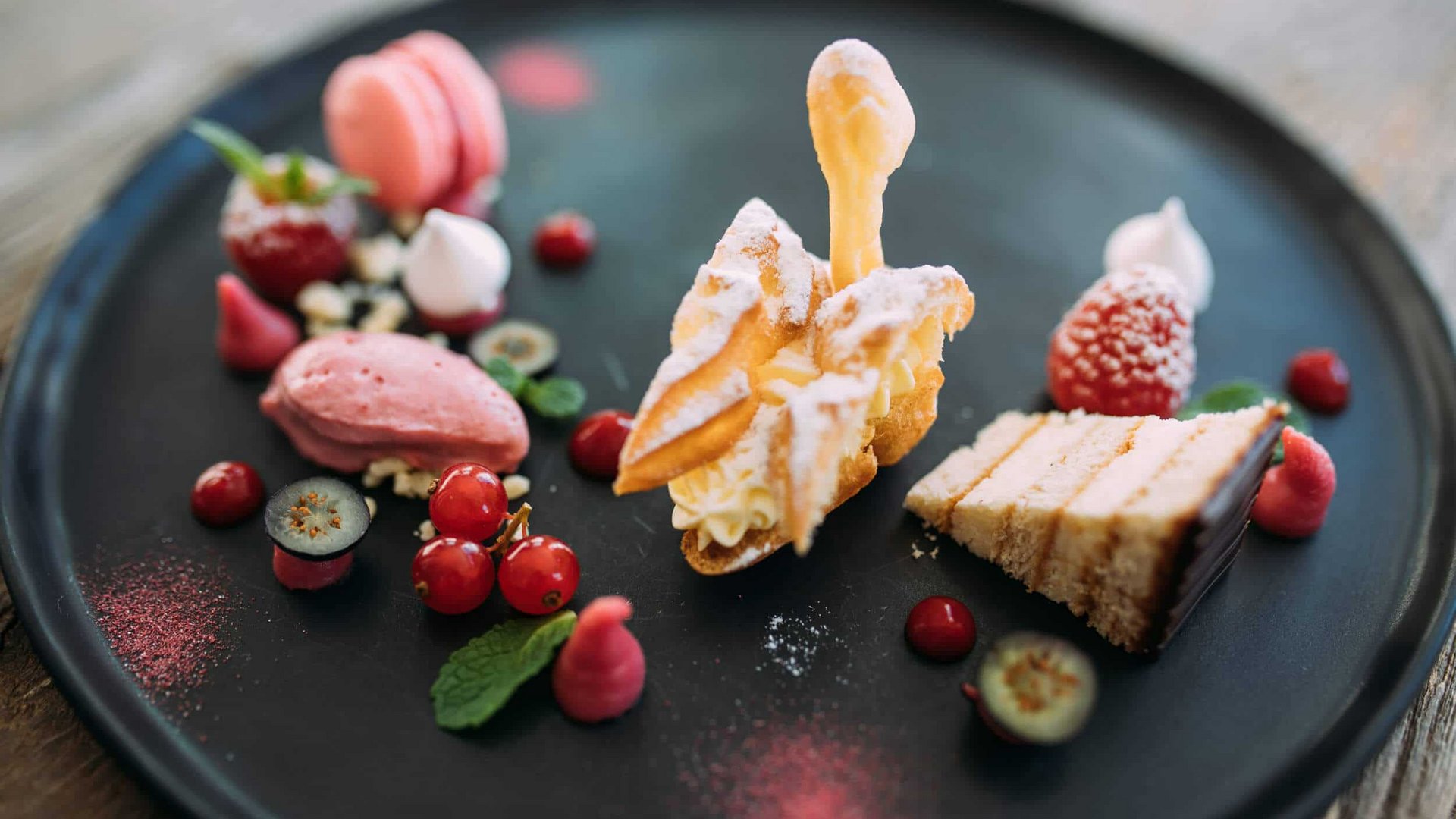 Assortment of fine desserts and fruits artfully arranged on a black plate