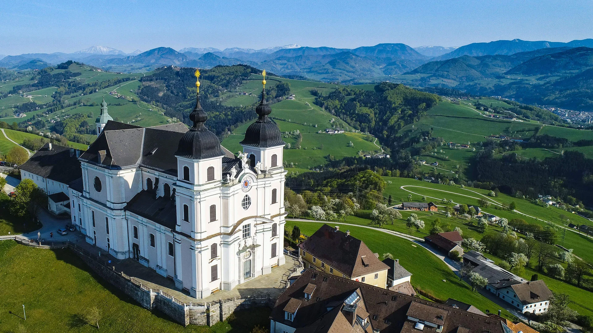 Weiße Kirche auf Hügel mit grünen Tälern und Bergen im Hintergrund
