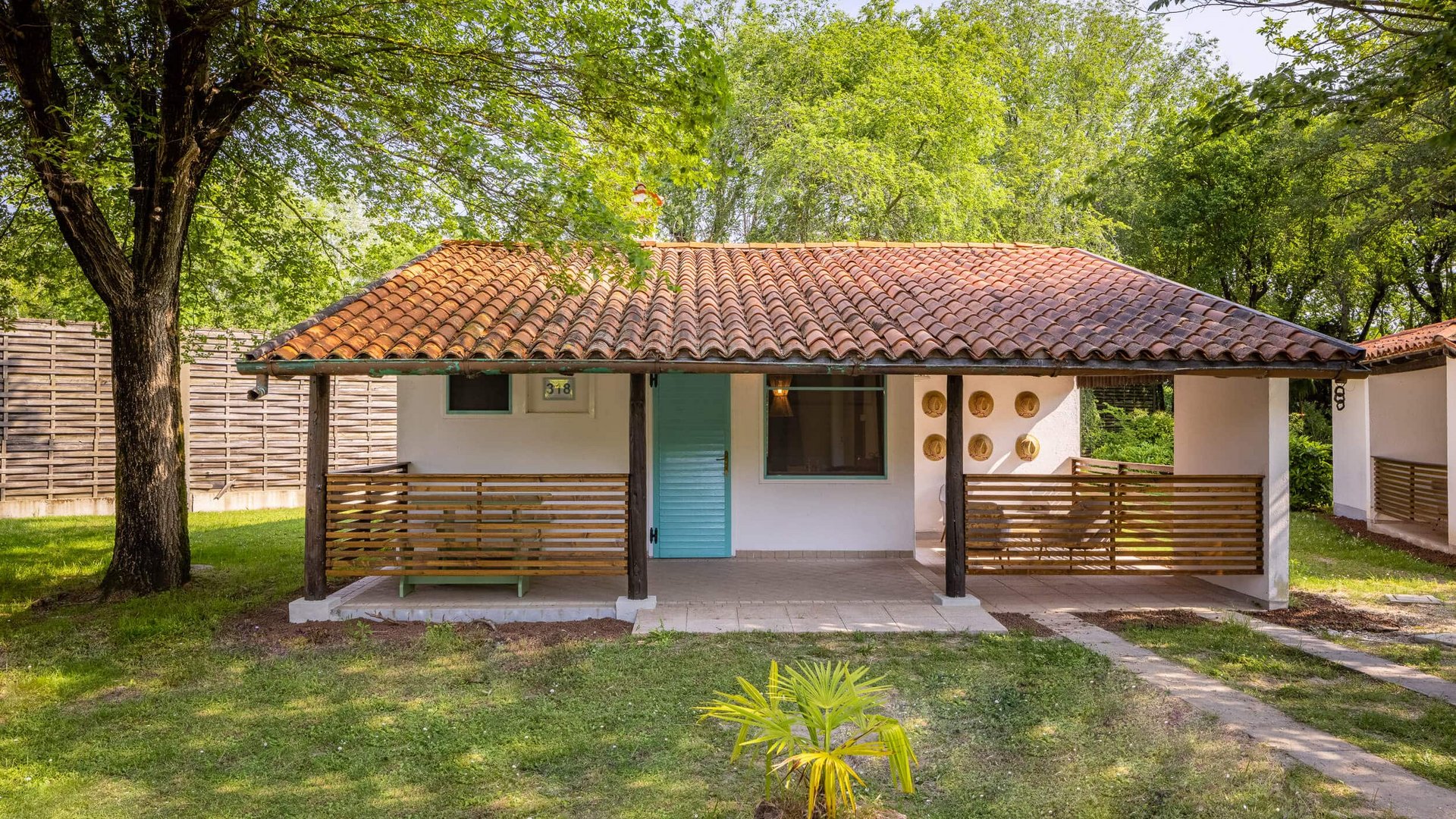 Small holiday house with porch and red tiled roof surrounded by trees