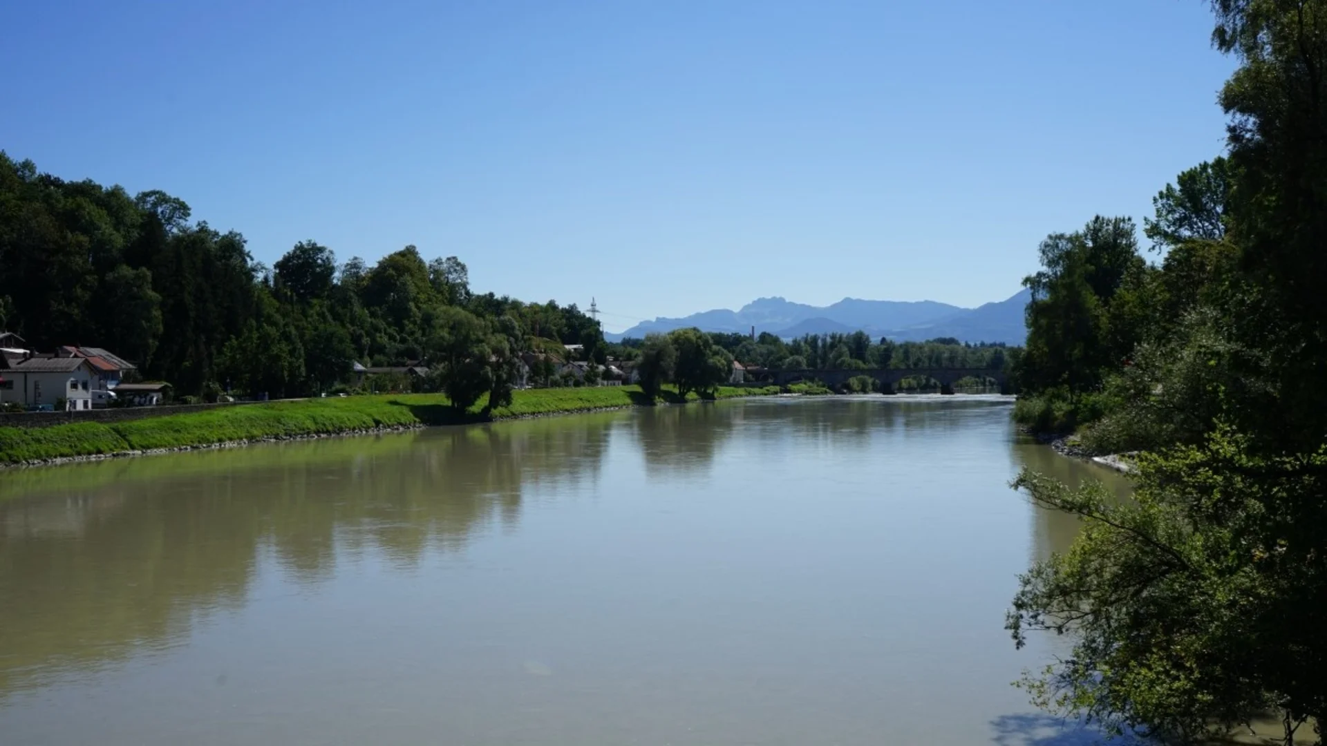 Fluss mit grünen Ufern und Bergen im Hintergrund unter klarem Himmel