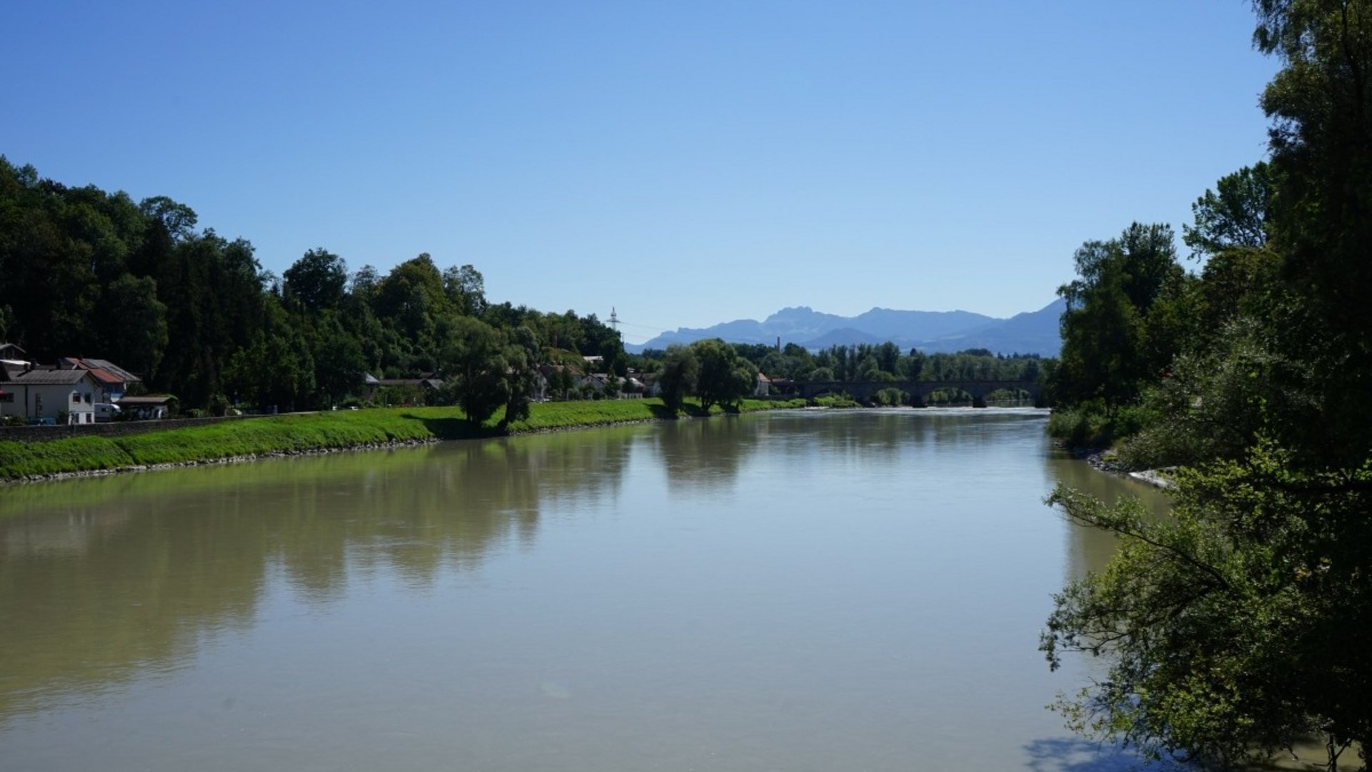 River with green banks and mountains in the background under clear sky