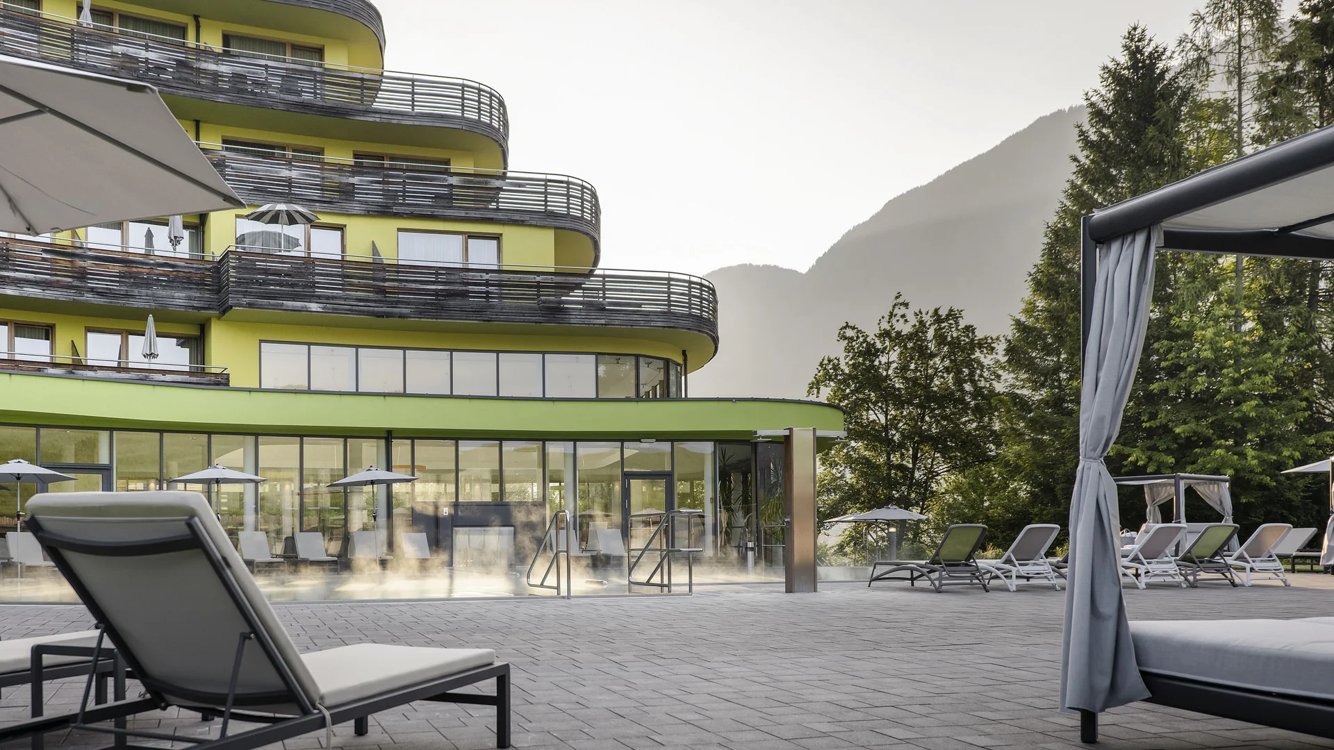 Hotelterrasse mit Liegestühlen vor modernem Gebäude und Berglandschaft