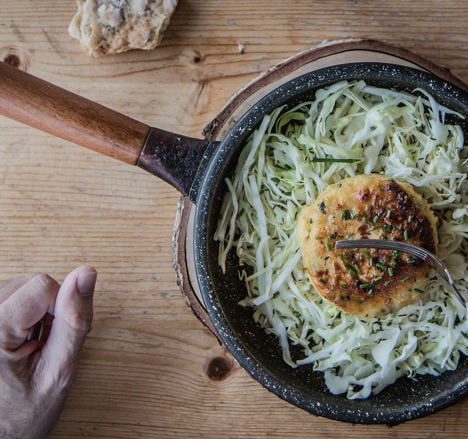Frying pan with fried veggie patty on cabbage salad and hand on wooden table