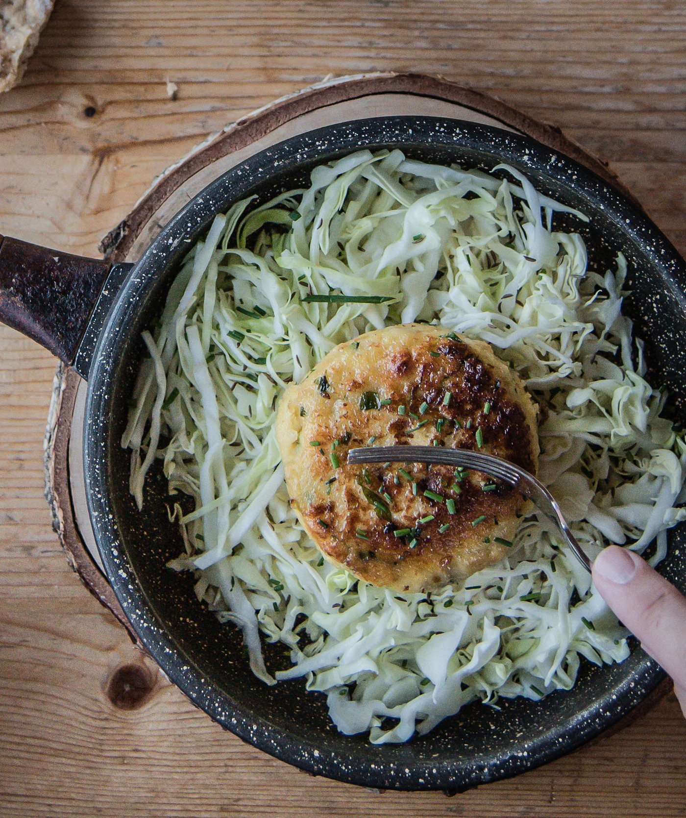 Frying pan with fried veggie patty on cabbage salad and hand on wooden table