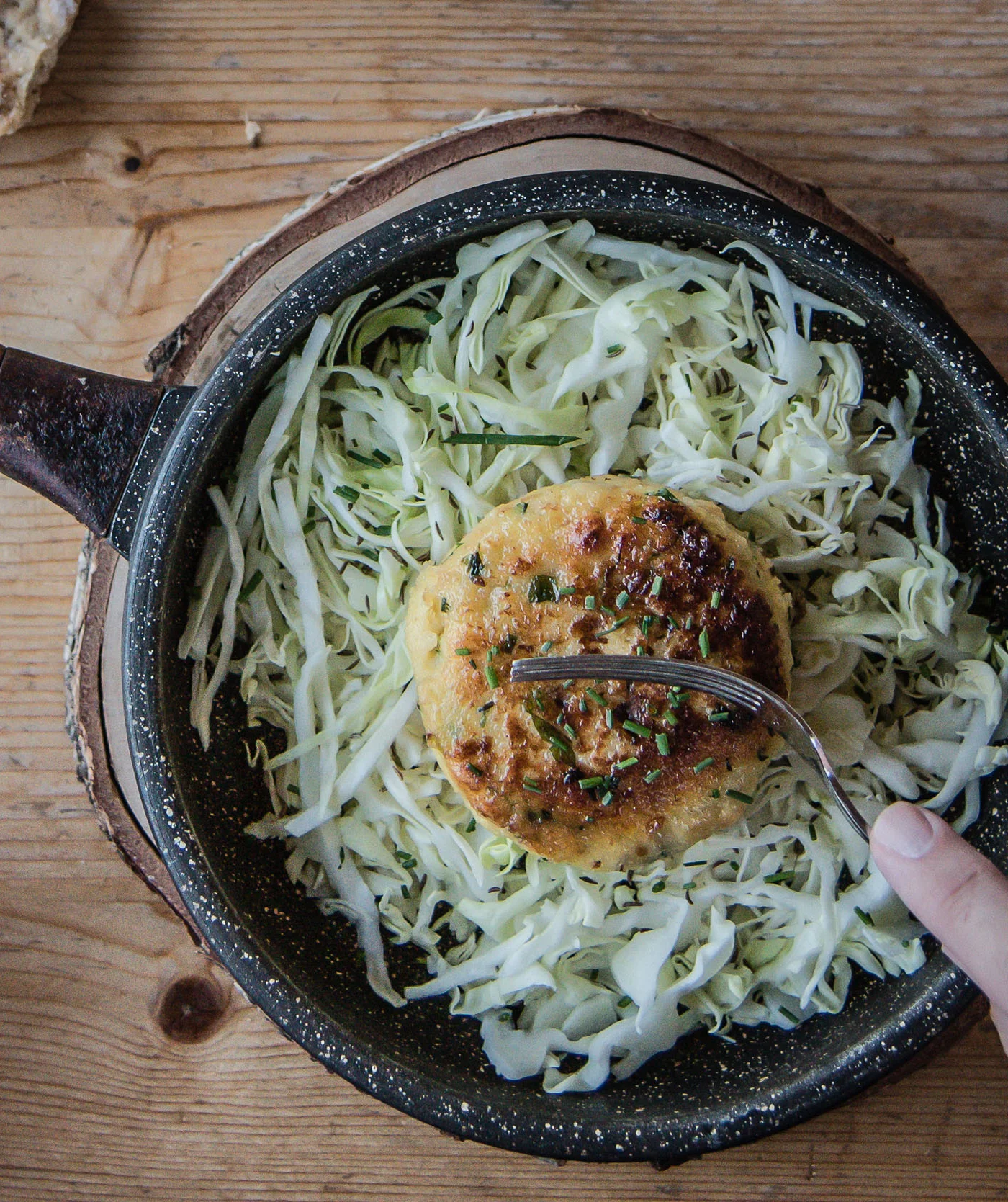 Koekenpan met gebakken vegetarische burger op koolsalade en hand op houten tafel