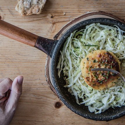 Frying pan with fried veggie patty on cabbage salad and hand on wooden table