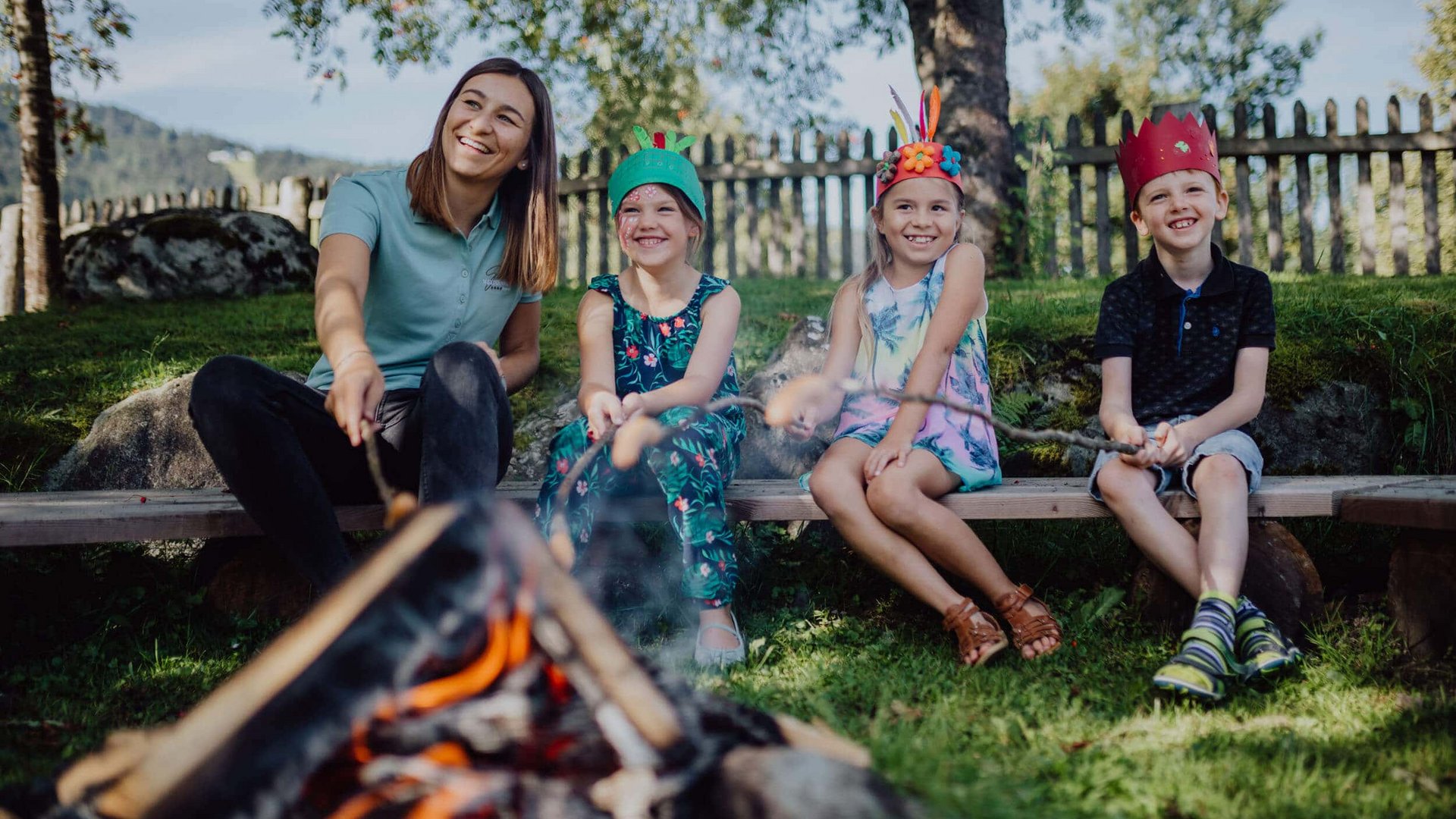 Woman and three children sitting by campfire roasting bread on sticks