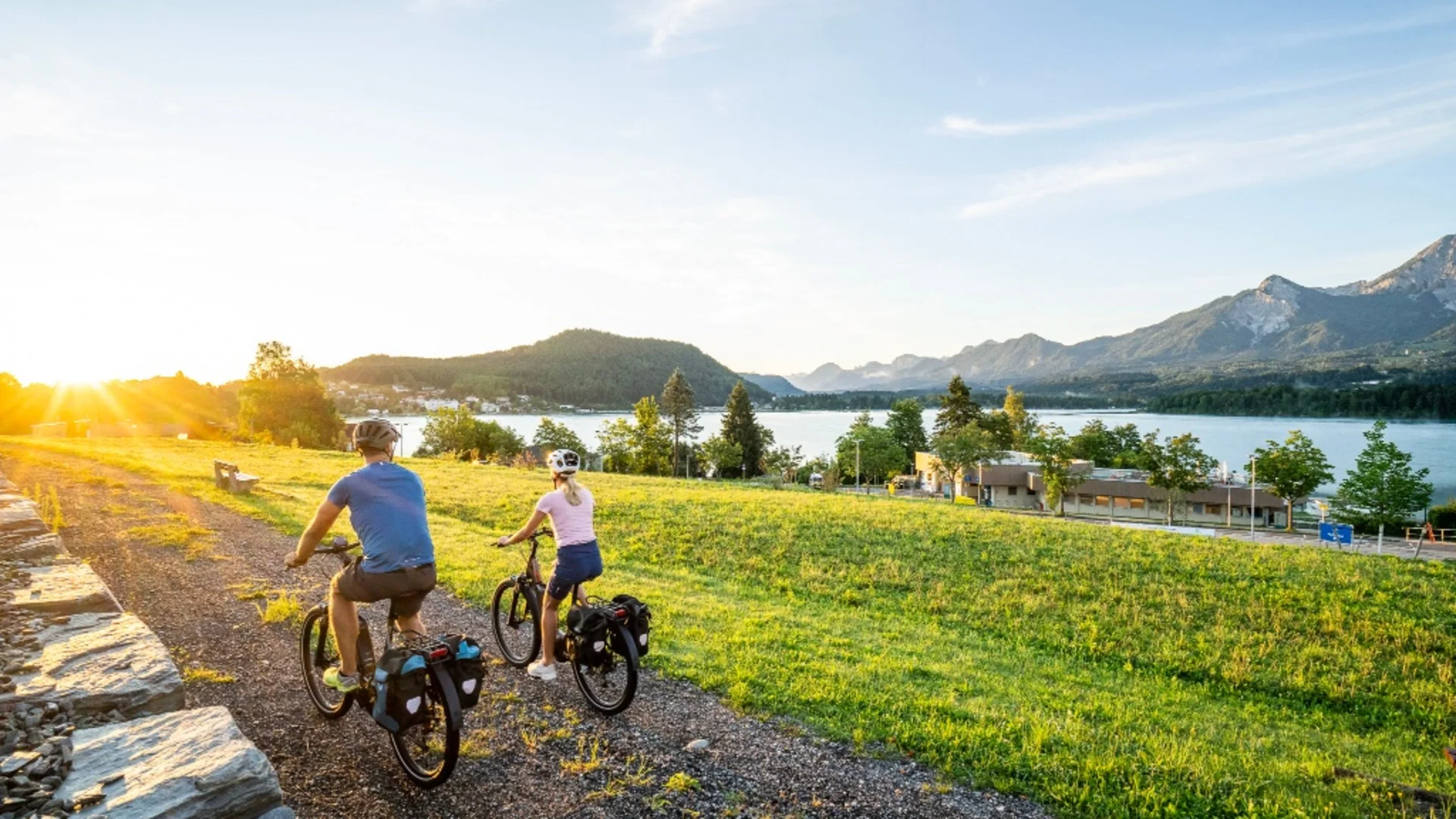 Twee fietsers op een pad langs meer en bergen bij zonsondergang