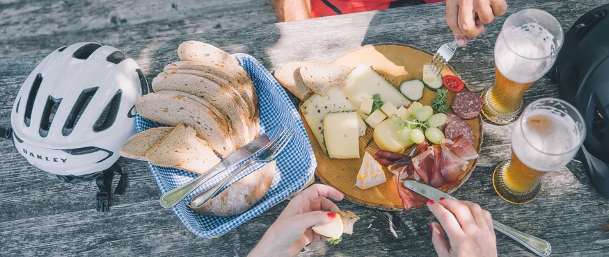Picknick met brood, kaas, vleeswaren en bier op houten tafel met fietshelmen