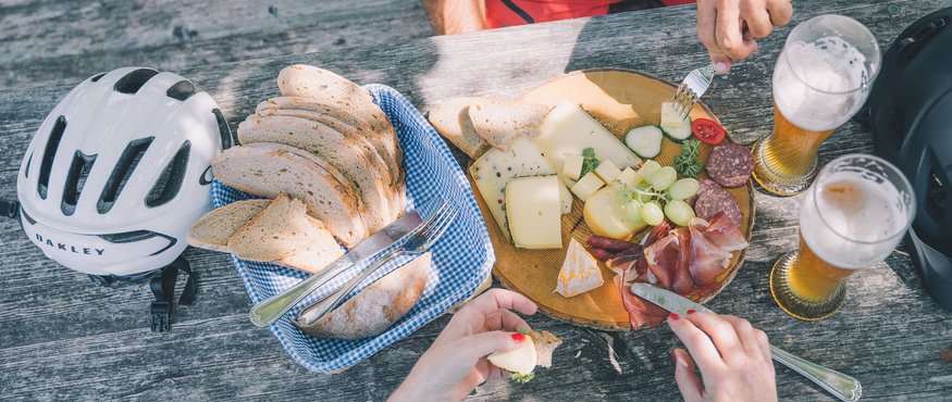 Radurlaub in Oberbayern © Tourismus Oberbayern München e.V. Picknick mit Brot, Käse, Aufschnitt und Bier auf Holztisch mit Fahrradhelmen