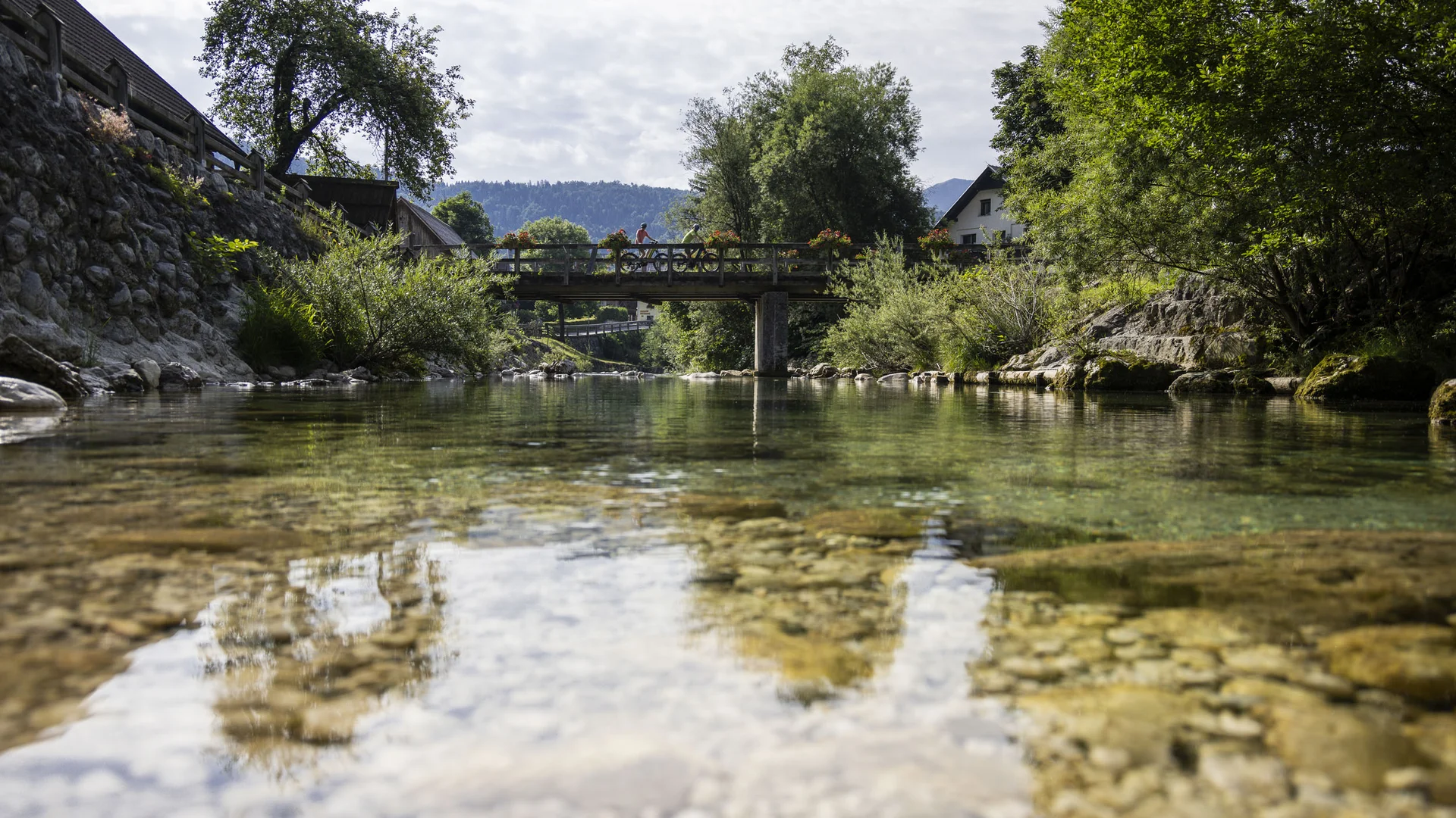 Doorzichtige rivier met brug en fietser in groene vallei