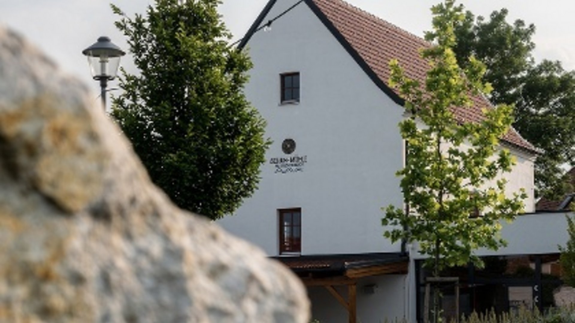 White house with red roof, trees, and an outdoor lamp in front