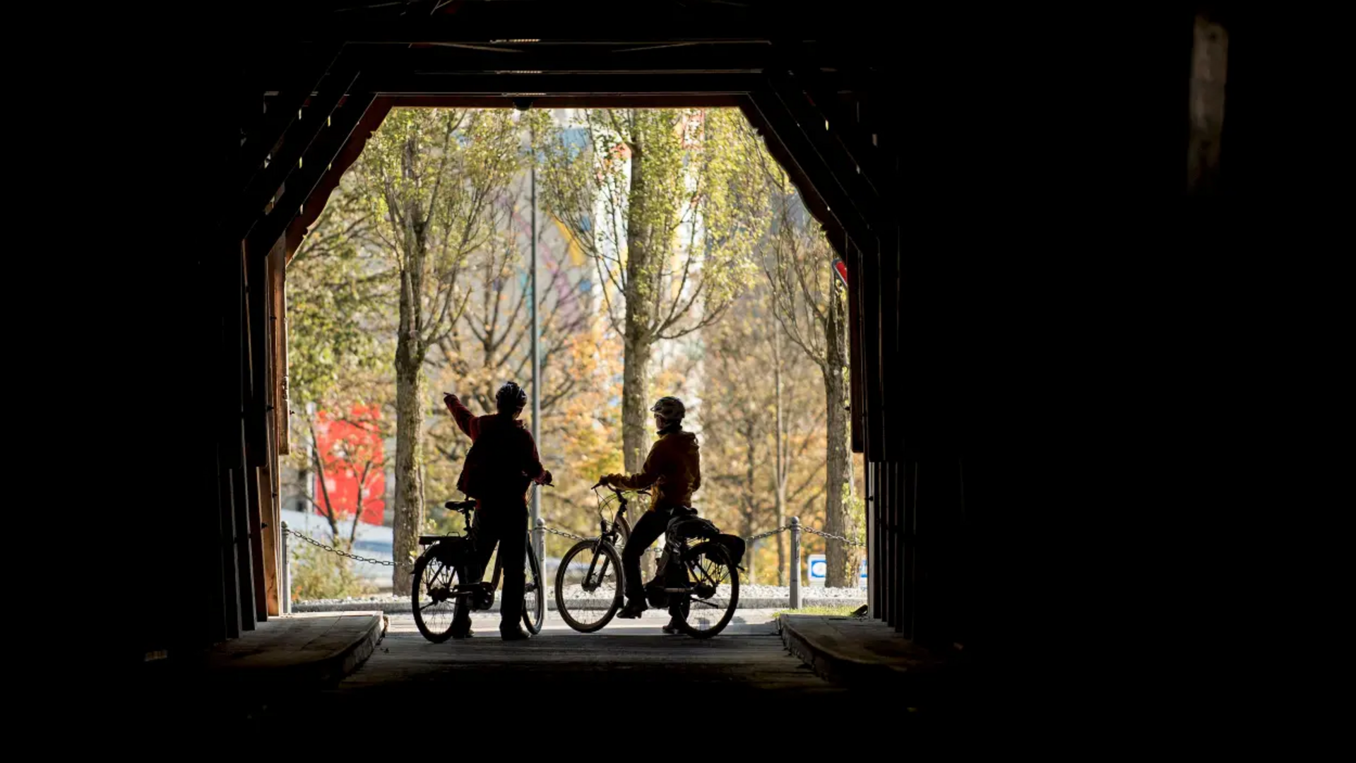 Two cyclists in a tunnel, one pointing outside at trees