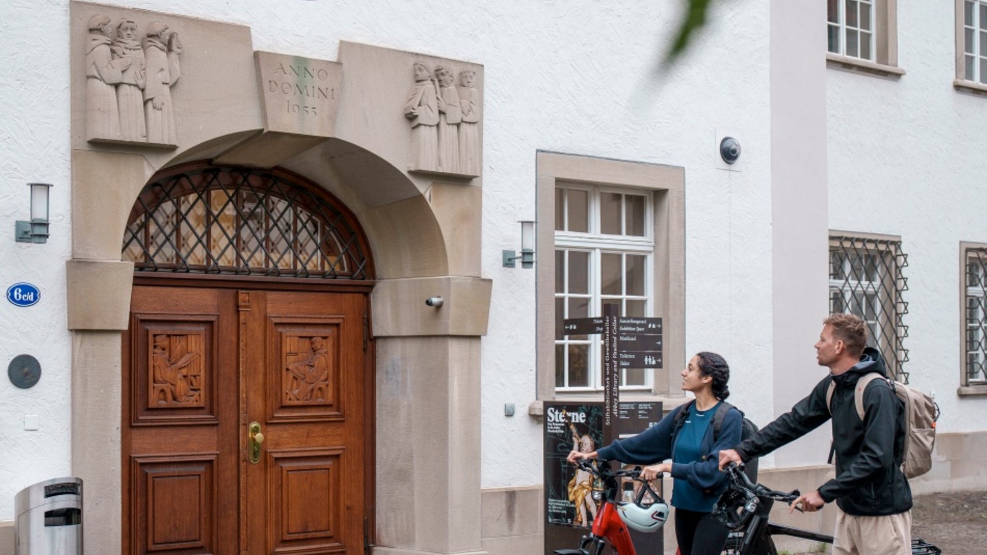 Two people with bikes in front of a historic building with wooden door