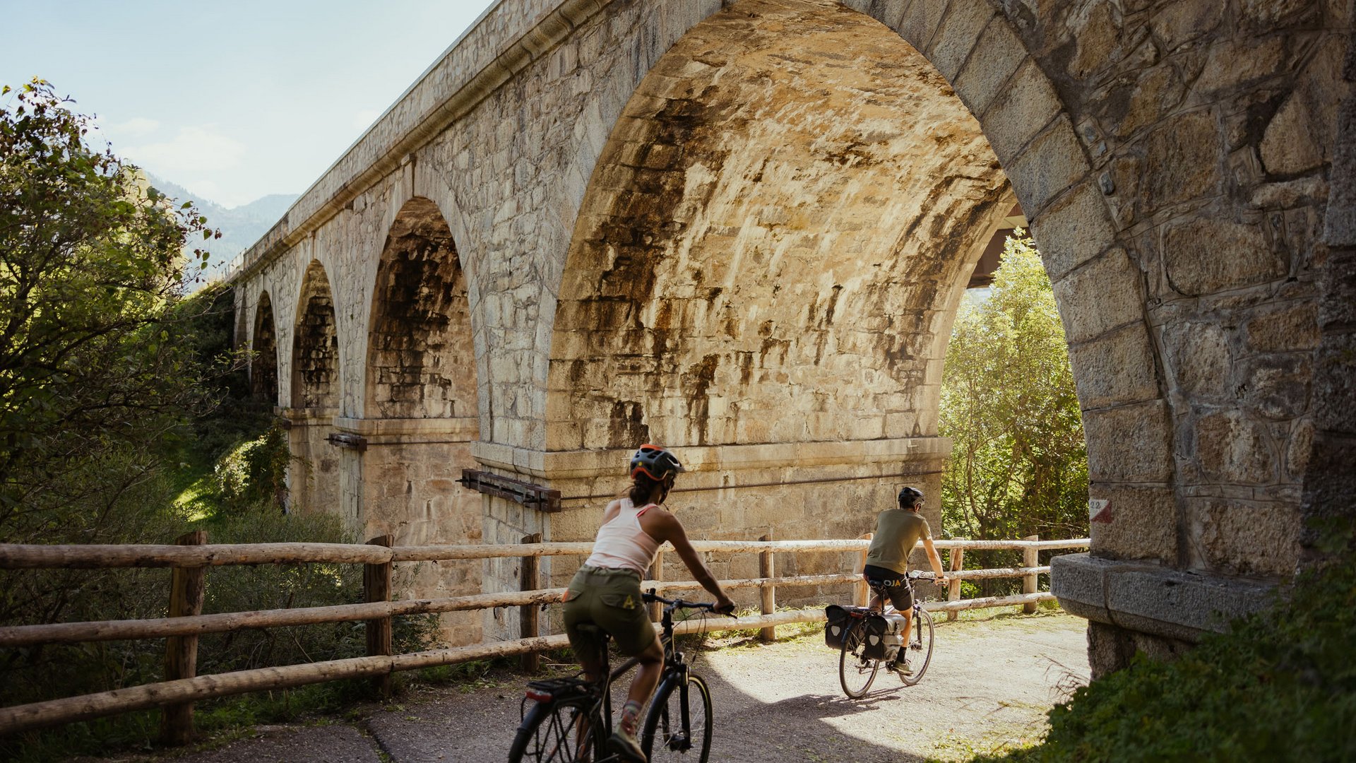 Two cyclists riding under a stone arch on a bike path