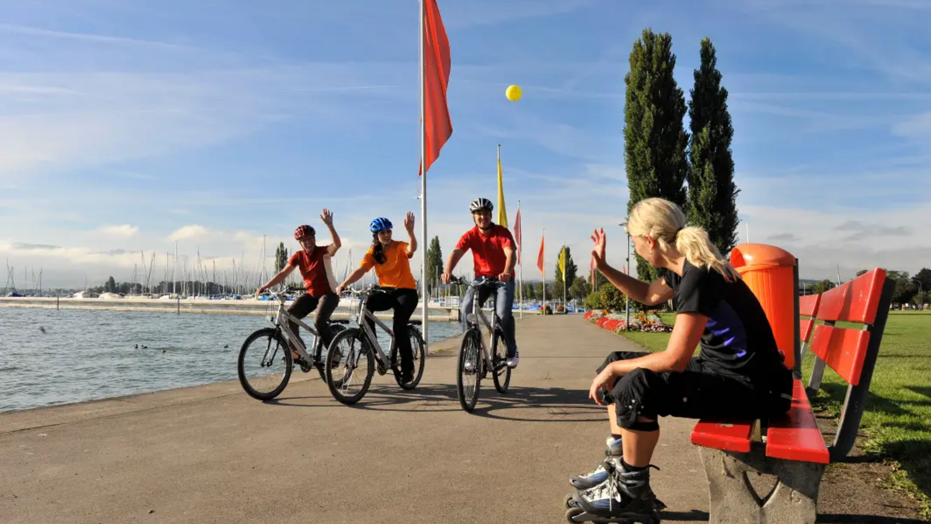 Woman on rollerblades greets three cyclists by the lakeside
