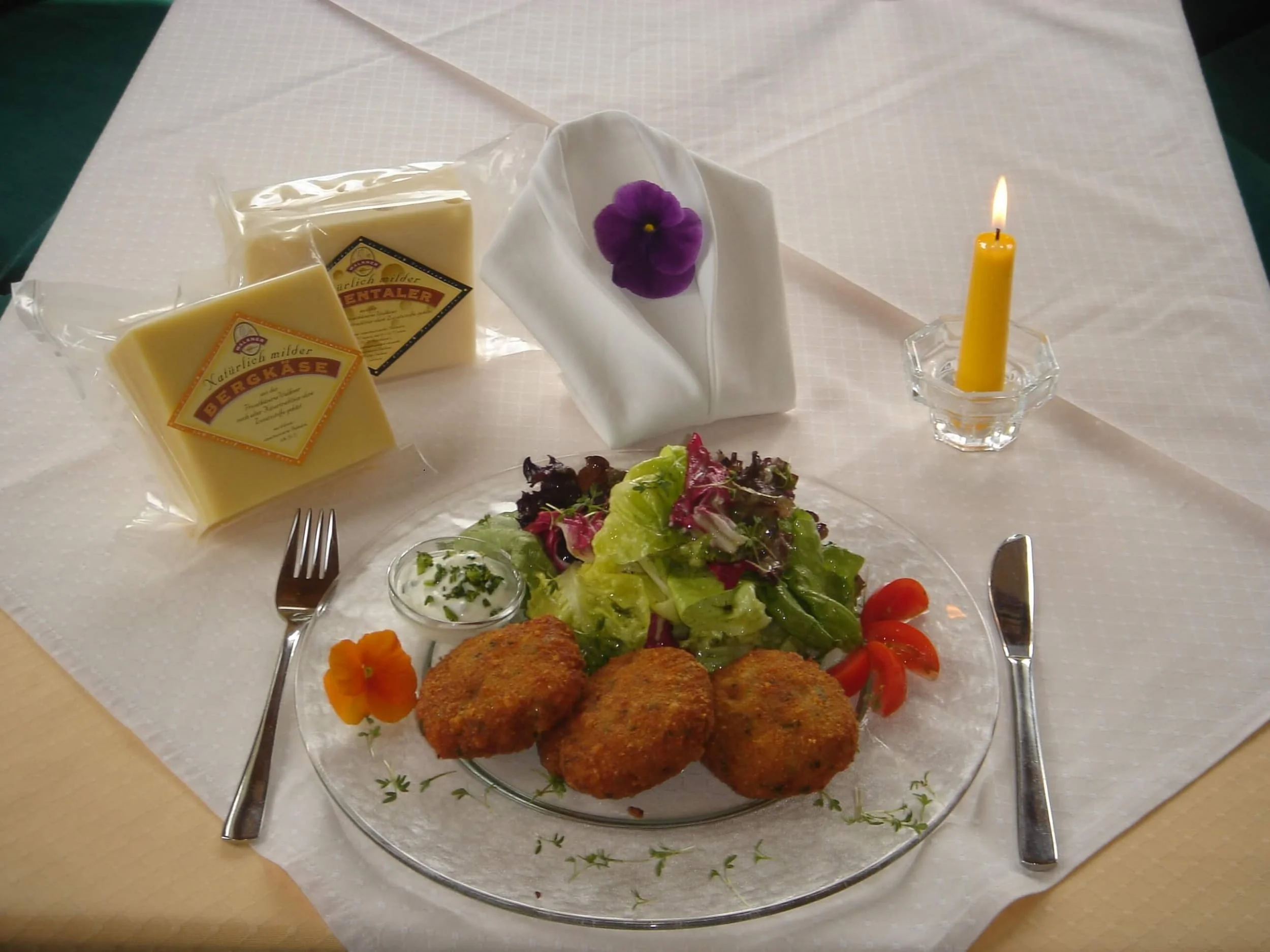 Bord met salade en drie gefrituurde kroketten, twee kaasblokken en een brandende kaars