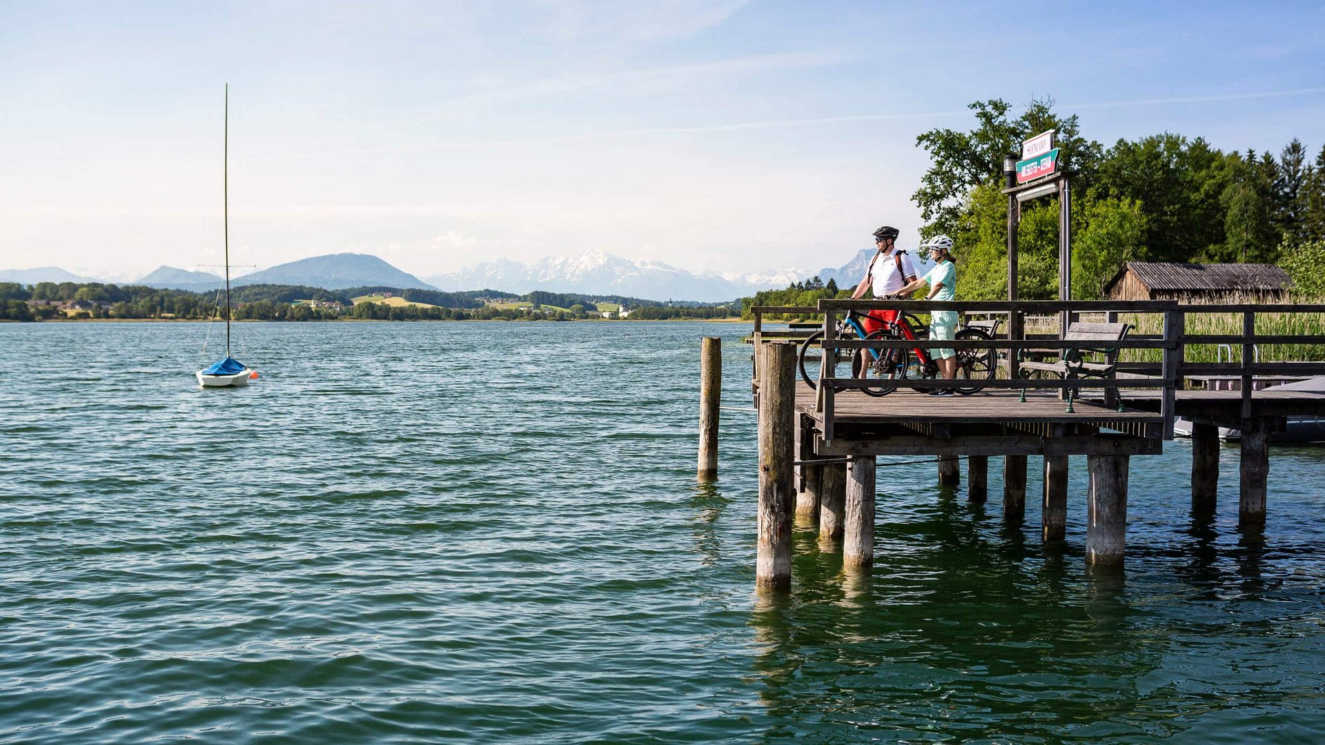 Two cyclists standing on a pier by the lake with mountain views on a clear day