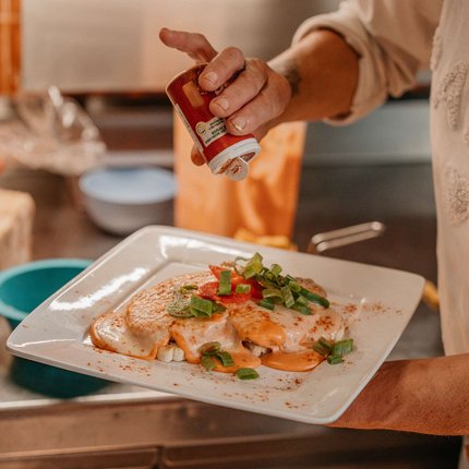 Hand sprinkling seasoning on dish with sauce and greens on a white plate