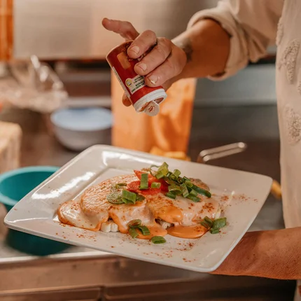 Hand strooit kruiden op gerecht met saus en groenten op een wit bord