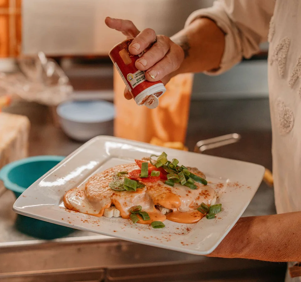 Hand strooit kruiden op gerecht met saus en groenten op een wit bord