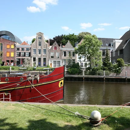 Rood schip aangemeerd aan rivier met historische huizen op de achtergrond