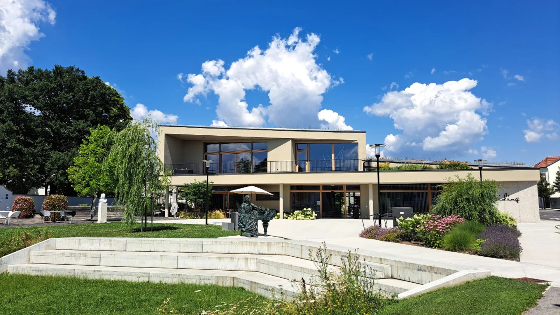 Modern gebouw met twee verdiepingen, tuin en zitgedeelte onder blauwe lucht