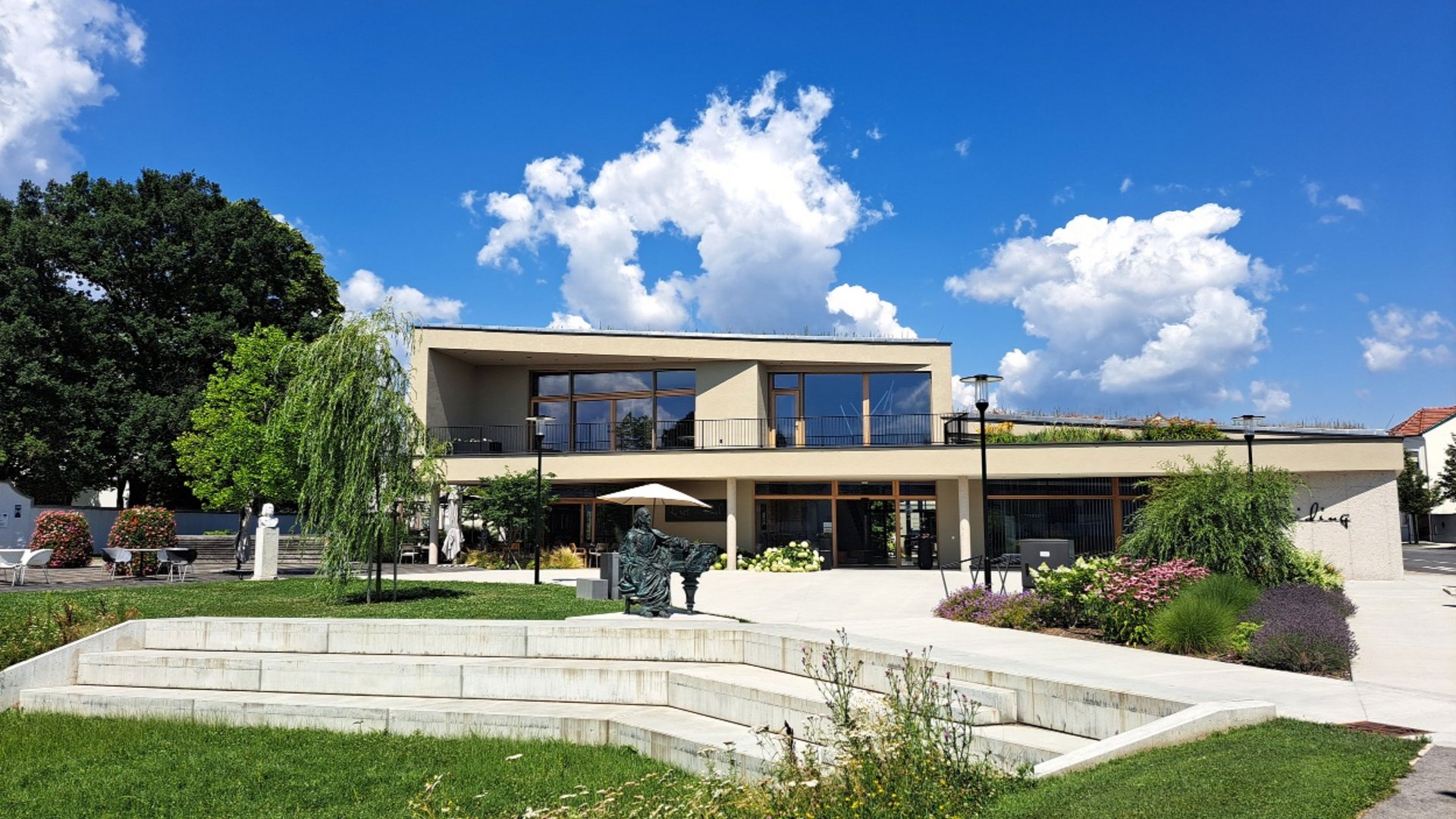 Modern two-story building with garden and seating area under blue sky