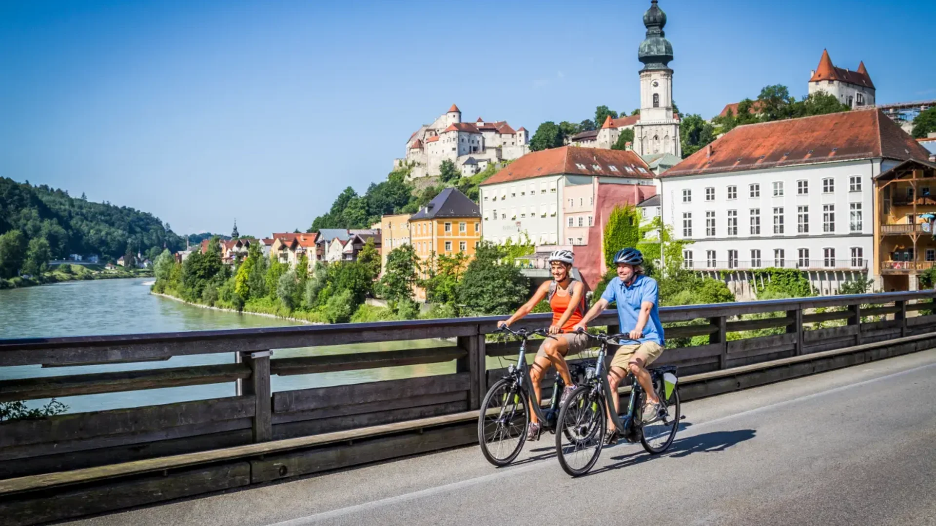 Zwei Radfahrer auf einer Brücke mit Blick auf eine Stadt und einen Fluss