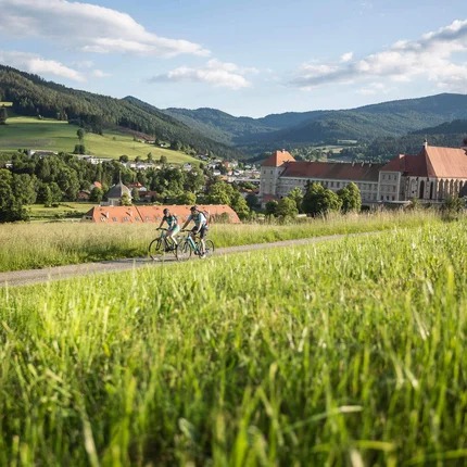 Twee fietsers op pad met groen veld en historisch klooster op de achtergrond